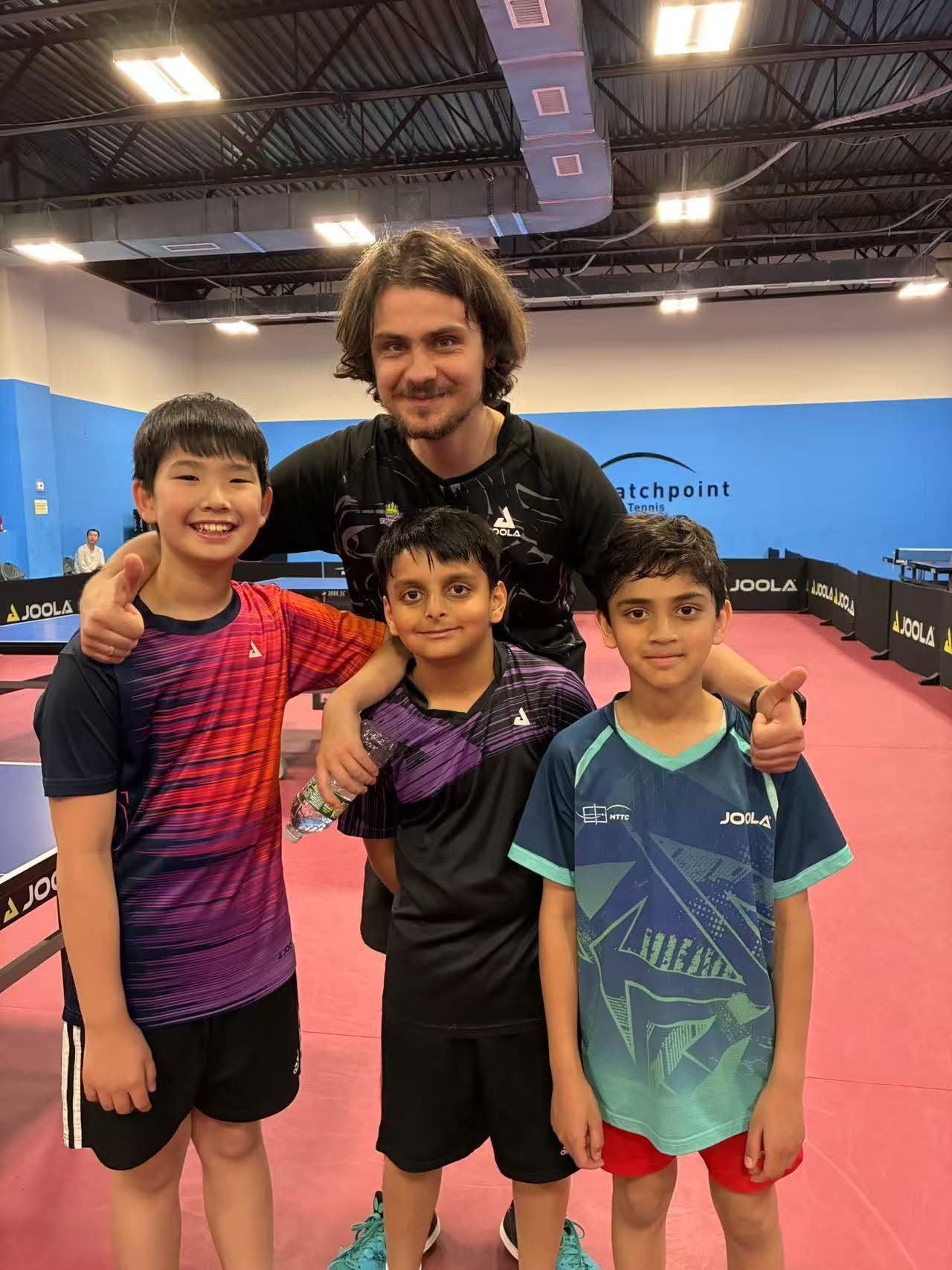 A coach and three young table tennis players posing together beside the tables.